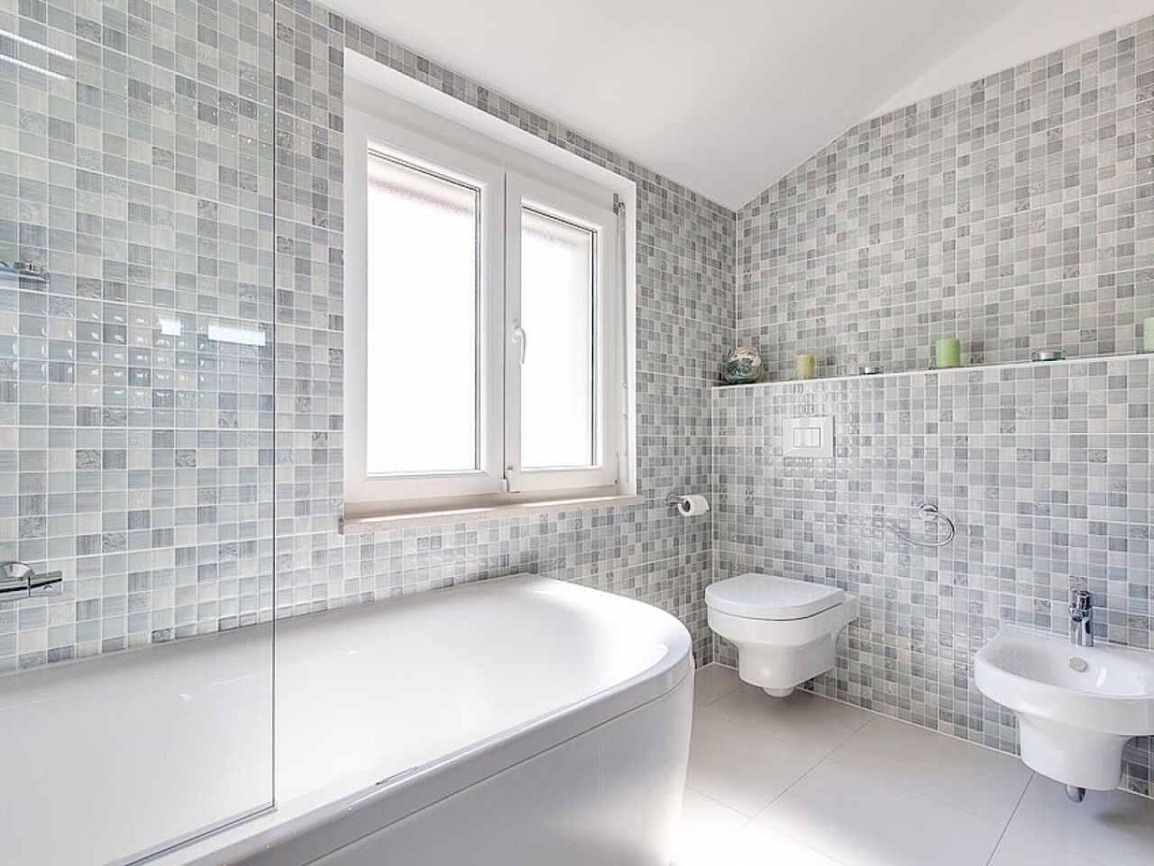 Mosaic-tiled bathroom with corner bathtub, toilet and bidet