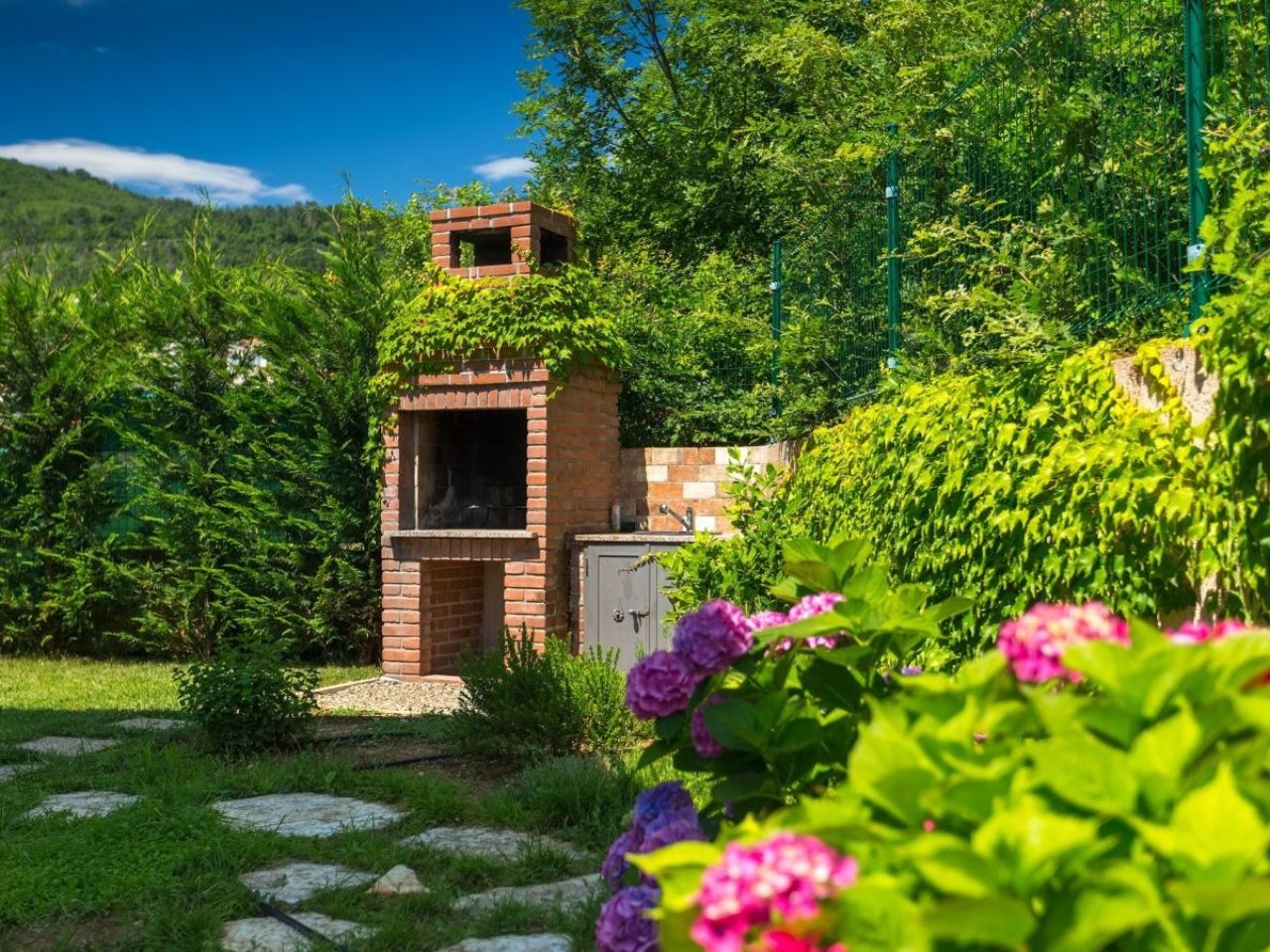Brick barbecue surrounded by lawn and flowering garden plants