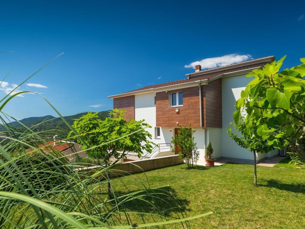 Rear villa facade and landscaped lawn beneath the wooded hills